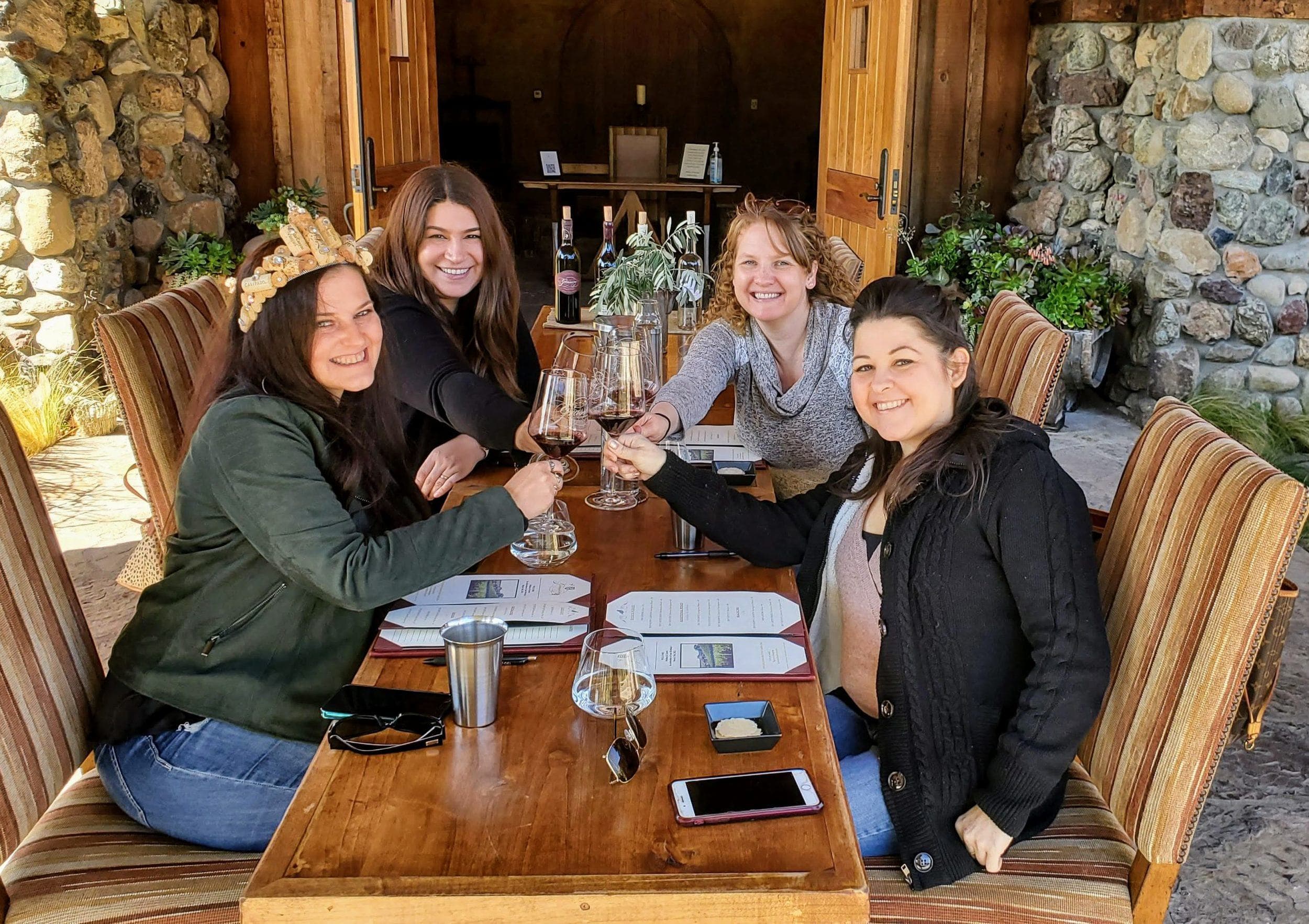 Four guests seated outdoors on a private wine-country tour, glasses raised